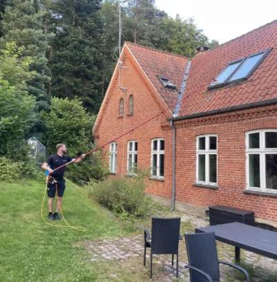 Domus pudser vinduer med rent-vand-stang på et rødt murstenshus med have